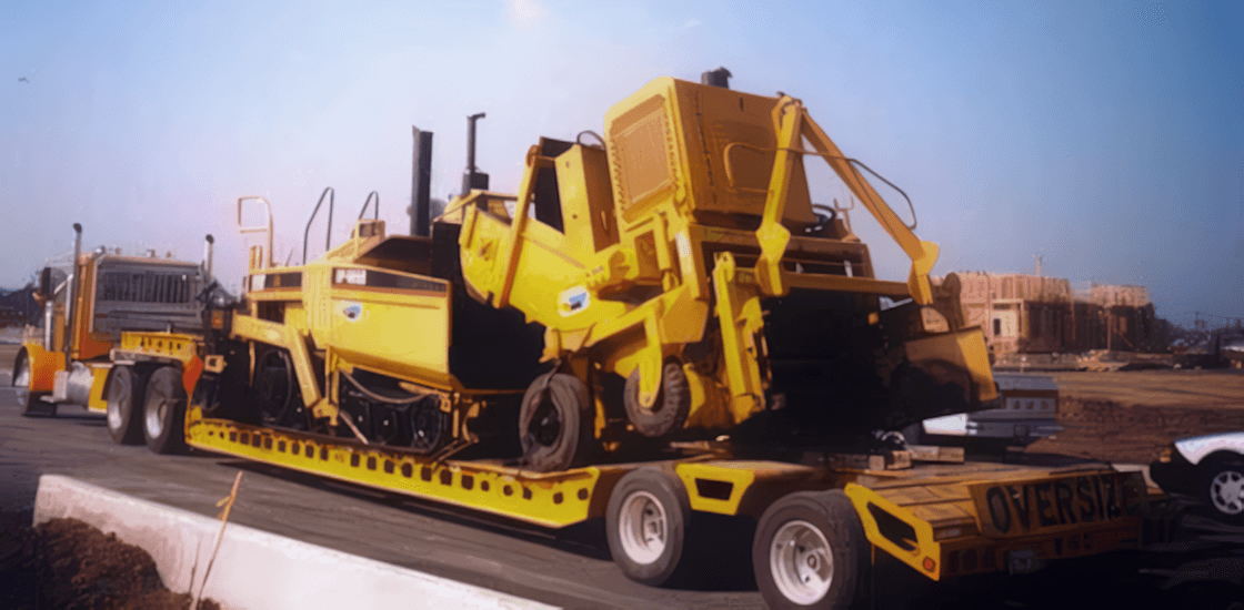 A yellow Muse Trucking truck hauling heavy machinery