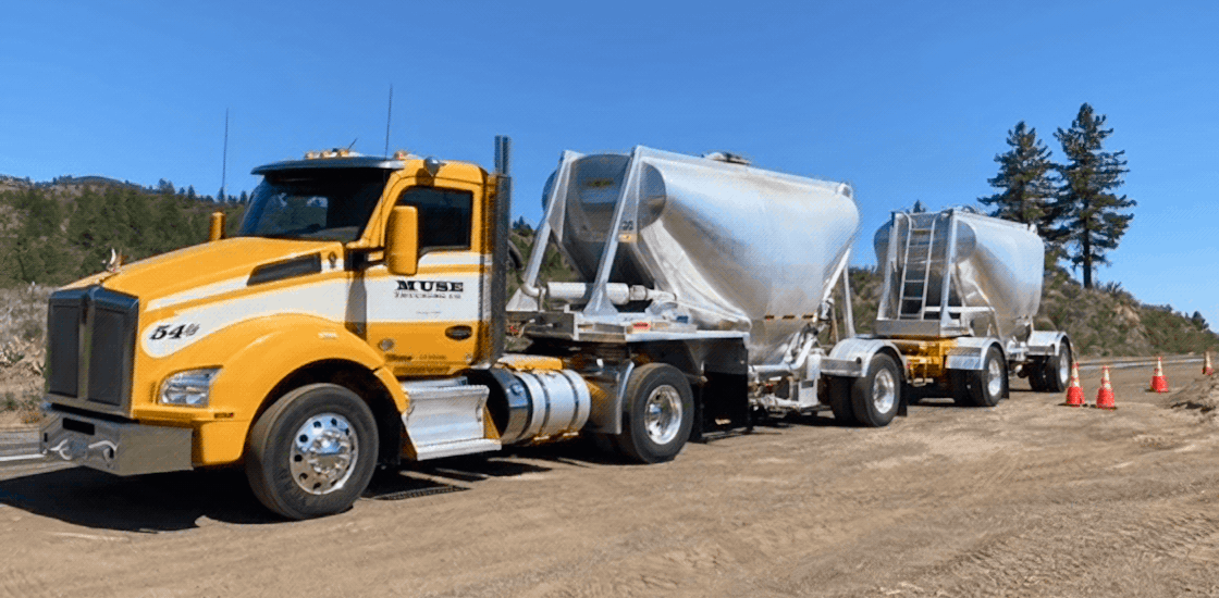 A yellow and white Muse Trucking truck hauling storage tanks