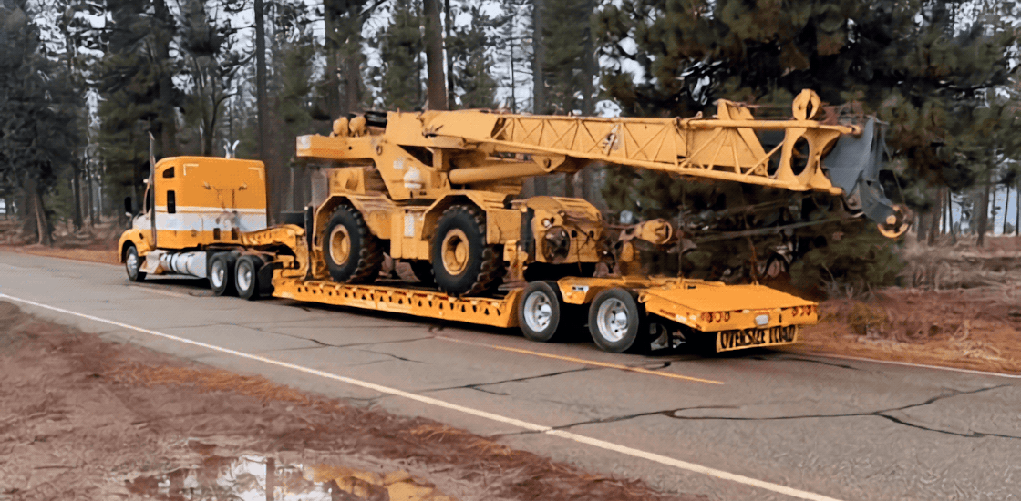 A yellow and white Muse Trucking truck hauling heavy machinery